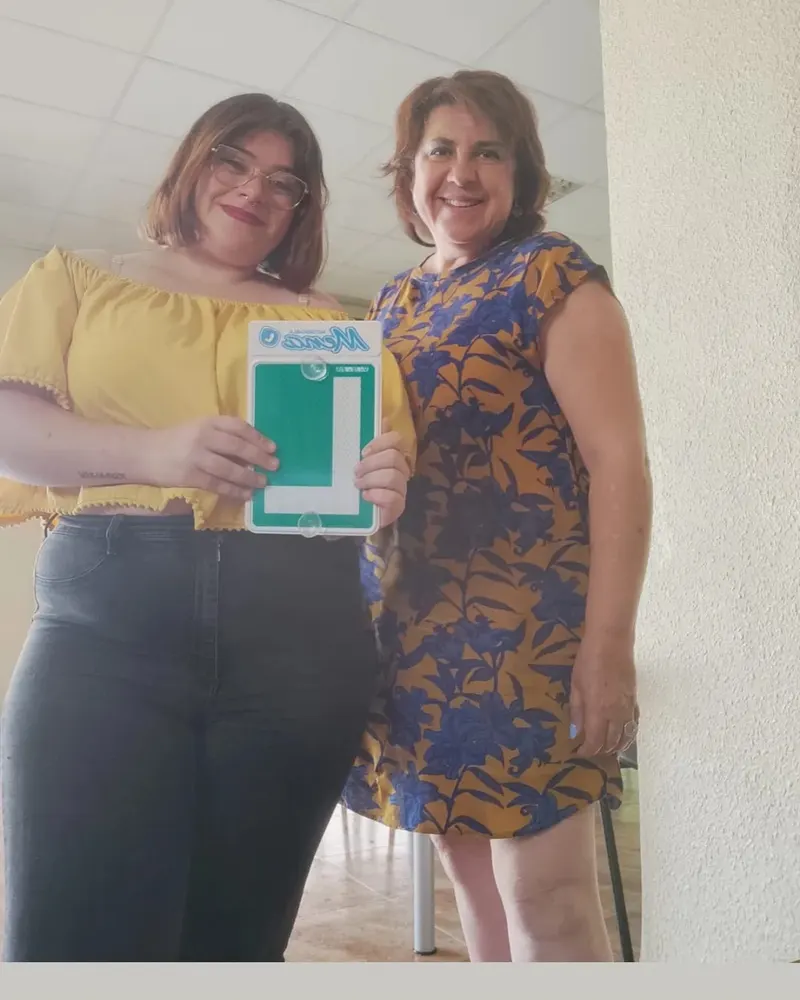 Una alumna y su profesora sonríen en el local de la autoescuela con la placa L de Mena